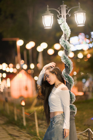 A young woman poses gracefully under a vintage street lamp, surrounded by soft glowing lights, emanating a sense of tranquility in a festive atmosphere.の写真素材