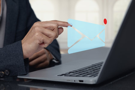 A professional person interacts with a floating email icon above a laptop, symbolizing digital communication in a modern workspace, emphasizing technology use.の写真素材