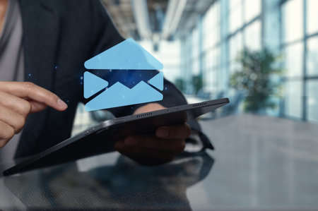 A businessperson interacts with a tablet featuring a floating email icon, symbolizing digital communication in a modern office setting.の写真素材