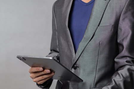 A stylish business professional in a gray suit holding a tablet, representing innovation and modern technology in a corporate environment. Perfect for business-related themes.の写真素材