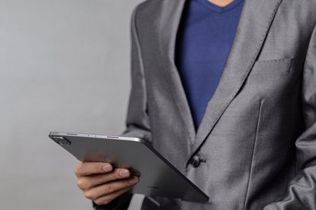A confident business professional wearing a suit holds a sleek tablet, showcasing modern technology in a stylish office environment. Perfect for corporate themes.の写真素材
