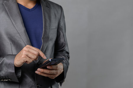 A business professional in a suit interacts with a smartphone, showcasing modern communication in a sleek gray background, representing contemporary work life.の写真素材