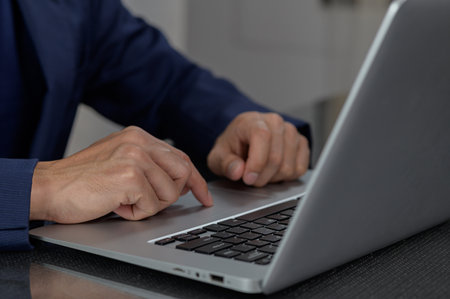 A business professional focuses on his laptop while engaged in work tasks. His attentive hands illustrate the importance of technology in the modern workspace.の写真素材