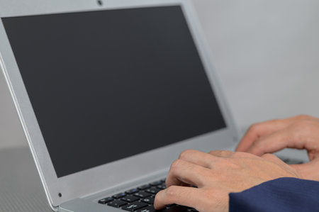 A close-up view showcasing hands typing on a laptop keyboard with a blank screen. This image represents modern technology and workspace productivity in a minimalistic setting.の写真素材
