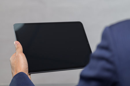 A professional man holds a blank tablet device in a modern office setting, symbolizing technology and innovation. The image conveys a focus on communication and productivity.の写真素材