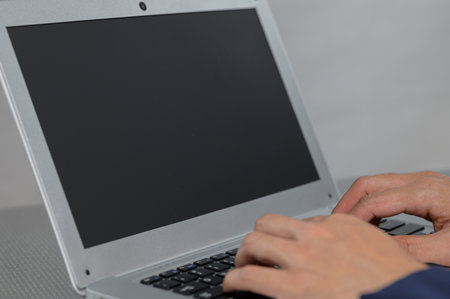 A close-up view of hands typing on a laptop keyboard with a blank screen. This image captures the essence of modern technology and productivity in a workspace setting.の写真素材