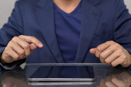 A businessman in a suit prepares to interact with a tablet on the table, showcasing focus and...