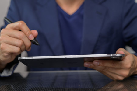 A professional man sits at a modern desk, using a tablet and stylus to enhance creativity and productivity in a contemporary office environment.の写真素材