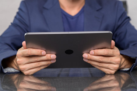 A close-up view of a person in professional attire holding a tablet in both hands. The scene...