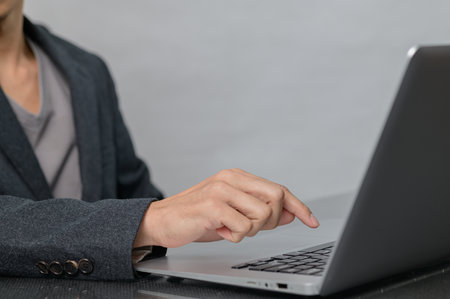 A focused individual dressed in professional attire engages with a laptop, showcasing modern technology in a workspace. Perfect for themes of business and productivity.の写真素材
