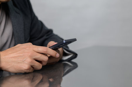 A close-up image of a person using a smartphone while sitting at a sleek table. The fingers interact with the device, showcasing a moment of modern communication.の写真素材