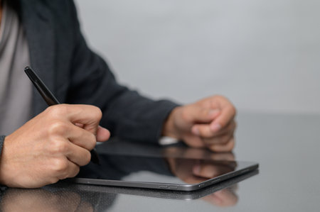 A focused individual writes notes on a sleek digital tablet using a stylus. The modern workspace reflects creativity and productivity, showcasing technology in action.の写真素材