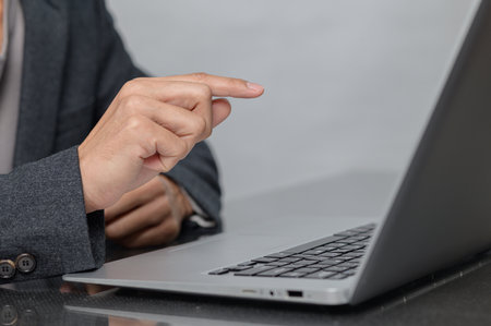 A business professional engages with a laptop in a modern workspace. The image showcases a focused hand pointing at the screen, highlighting technology use.の写真素材