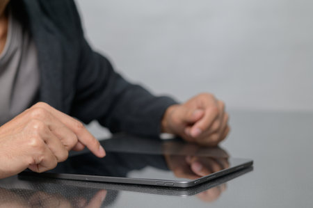 A close-up view of a person using a tablet device with one hand, highlighting a digital interaction. The modern workspace reflects a seamless blend of technology and productivity.の写真素材