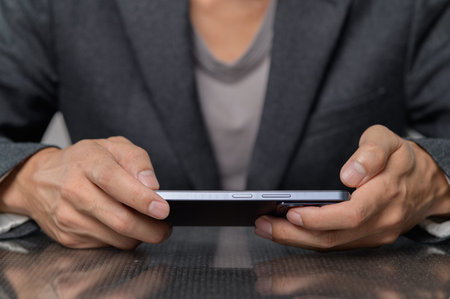 A businessman in a formal suit holds a smartphone with both hands. The image captures a close-up...