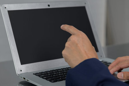 A close-up view of a person's hand gesturing towards a blank laptop screen, suggesting interaction...