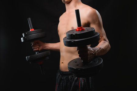 A shirtless athlete demonstrates strength while lifting dumbbells, showcasing physical fitness and health. The black background emphasizes focus and effort in the workout.の写真素材