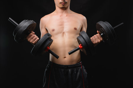 A muscular man displays his strength by lifting dumbbells, emphasizing the dedication to fitness and health. The image captures the essence of athleticism and determination.の写真素材
