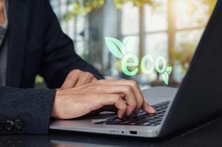 A close up of hands typing on a laptop in a modern workspace, featuring an eco friendly symbol. This image embodies the connection between technology and sustainability, promoting green business practices.の写真素材