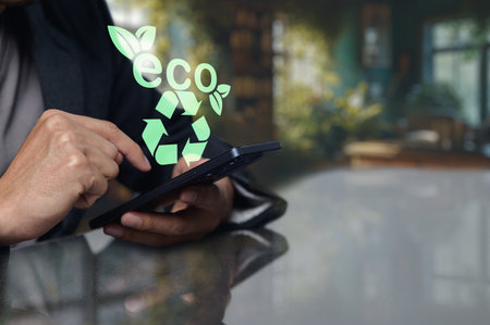 A close up view of a hand using a smartphone, showcasing eco friendly symbols like leaves and recycling icons. Emphasizes the importance of sustainable technology and innovation.の写真素材