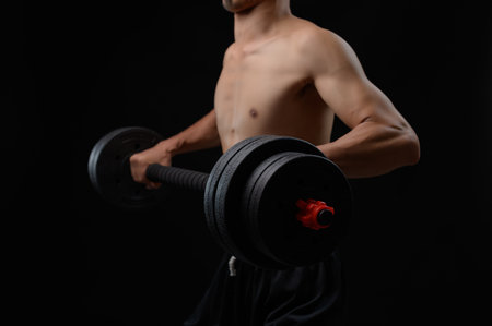 A shirtless man engages in strength training with a dumbbell, emphasizing physical fitness and health. The dramatic lighting showcases muscle definition and determination in his workout.の写真素材