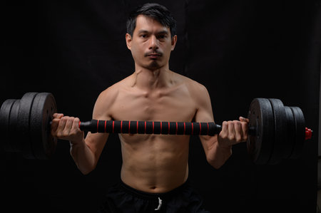 A dedicated male athlete performs weightlifting to enhance strength and health. His focused expression reflects determination in achieving fitness goals. Ideal for fitness-themed content.の写真素材
