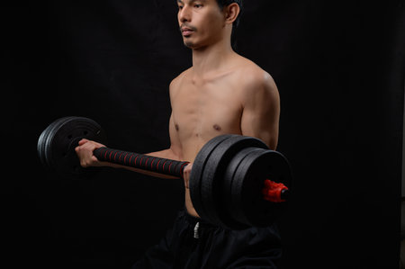 A focused man lifts a heavy dumbbell in a dark gym, showcasing strength and dedication to fitness.の写真素材