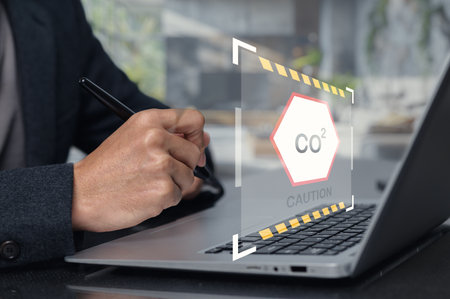 A professional examines carbon dioxide measurement technology on a laptop. The caution symbol highlights the importance of monitoring air quality in the workspace.の写真素材