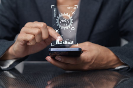 A professional individual interacts with a smartphone displaying data related to carbon dioxide emissions, emphasizing technology's role in environmental management and sustainability.の写真素材
