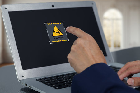 A person interacts with a laptop displaying a caution sign for carbon dioxide levels. The image underscores the importance of monitoring air quality and safety.の写真素材
