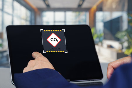 A modern office scene featuring a person pointing at a digital tablet displaying a caution sign for carbon dioxide. The image emphasizes workplace safety and awareness.の写真素材