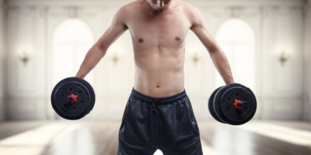 A determined male athlete lifts dumbbells in a bright gym, showcasing strength and focus. Perfect for themes of fitness, motivation, and athletic performance.の写真素材