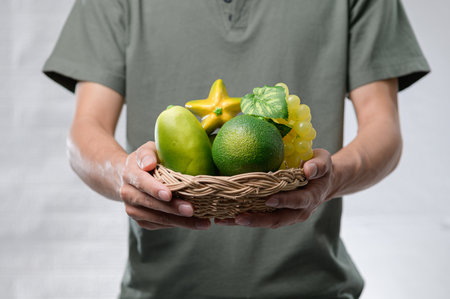 A person holds a woven basket filled with an assortment of fresh organic fruits, showcasing vibrant colors and promoting a healthy lifestyle choice.の写真素材