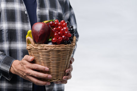 A person holds a woven basket filled with a variety of fresh fruits, symbolizing healthy living and nutritious choices. Explore the beauty of nature's bounty.の写真素材