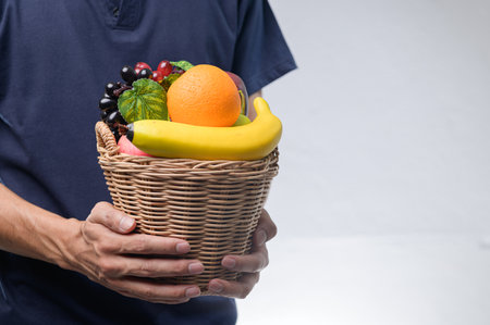A close-up image showcasing a person holding a wicker basket filled with a variety of fresh fruits, including bananas, grapes, and oranges.の写真素材
