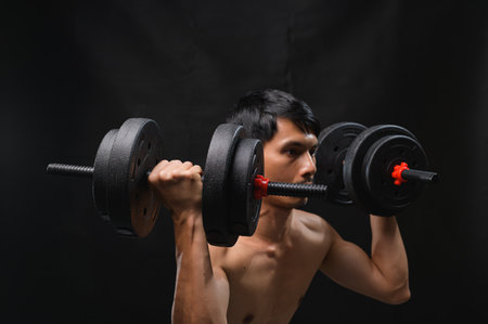 A young man is engaged in weightlifting, focusing on building strength and improving health. His determination is evident as he lifts heavy weights in a gym setting.の写真素材