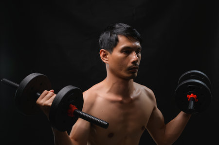 A young man is lifting dumbbells to enhance his strength and health. This image captures determination and dedication in fitness training, showcasing the athletic physique.の写真素材