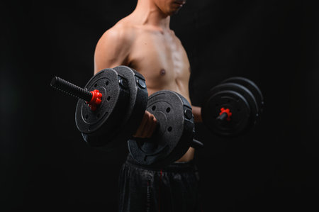 A fit individual performs a strength training exercise with dumbbells. The dim background highlights the focus on physical fitness and muscle building. Ideal for health and workout themes.の写真素材