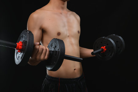A young man engages in strength training by lifting dumbbells in a dark gym. The image captures the essence of fitness, health.の写真素材