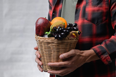A person holds a wicker basket filled with fresh organic fruits, showcasing vibrant colors against a soft background, perfect for promoting healthy living and nutrition.の写真素材