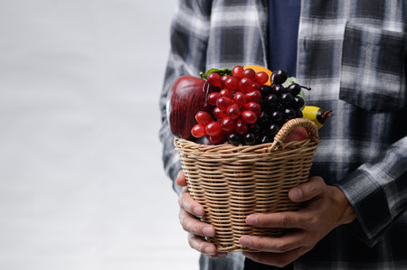 A person holds a wicker basket filled with a variety of fresh fruits, showcasing vibrant colors, emphasizing healthy eating and natural ingredients.の写真素材