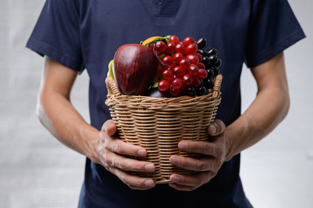 A man presents a woven basket filled with fresh fruits and vegetables, showcasing a vibrant selection rich in color and nutrition, perfect for healthy living.の写真素材