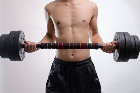 A young man engages in a strength training workout, lifting heavy dumbbells. This image captures the dedication and energy required for fitness, showcasing upper body strength and commitment to a healthy lifestyle.の写真素材