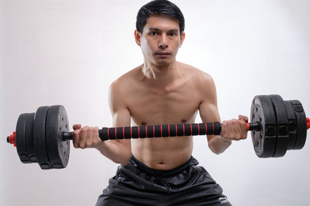 A young man showcases his strength and determination while lifting dumbbells in a fitness setting. This image emphasizes physical training and health.の写真素材