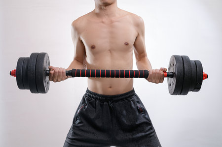 A strong man demonstrates his dedication to fitness by lifting a heavy dumbbell in a gym. The intensity of his workout showcases strength and determination in an athletic environment.の写真素材