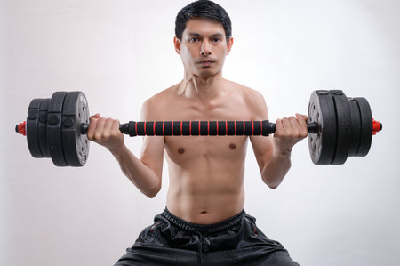 An athletic man is lifting a heavy dumbbell in a fitness studio, showcasing his commitment to strength training and physical fitness. Perfect for health-related themes.の写真素材