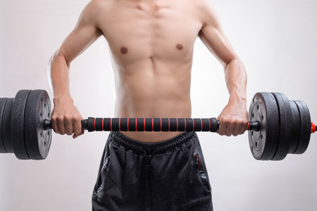 A young man demonstrates strength and focus while lifting a heavy dumbbell in a training session. This image captures the essence of determination and fitness.の写真素材