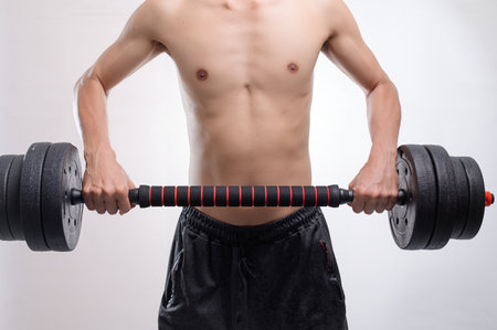 A young man's upper body shows strength as he lifts a heavy dumbbell, embodying dedication to fitness and athleticism. The image captures motivation and energy in a gym setting.の写真素材