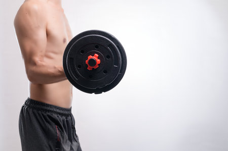 A focused man is lifting a dumbbell in a minimalist gym setting, emphasizing fitness and strength. His toned torso showcases commitment to a healthy lifestyle.の写真素材
