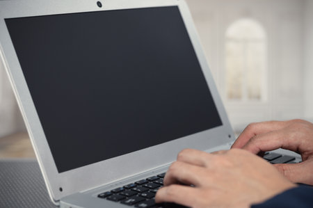 A close-up image of hands typing on a sleek laptop with a blank screen, situated in a minimalist workspace. Ideal for illustrating themes of technology and productivity.の写真素材